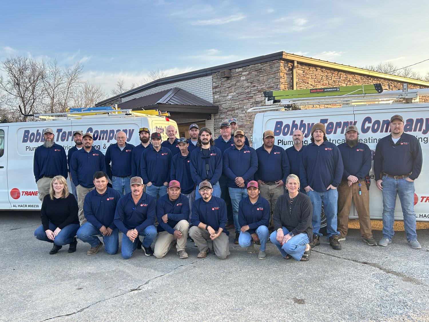 Plumbing and HVAC service team in branded uniforms posing in front of Bobby Terry Company vans